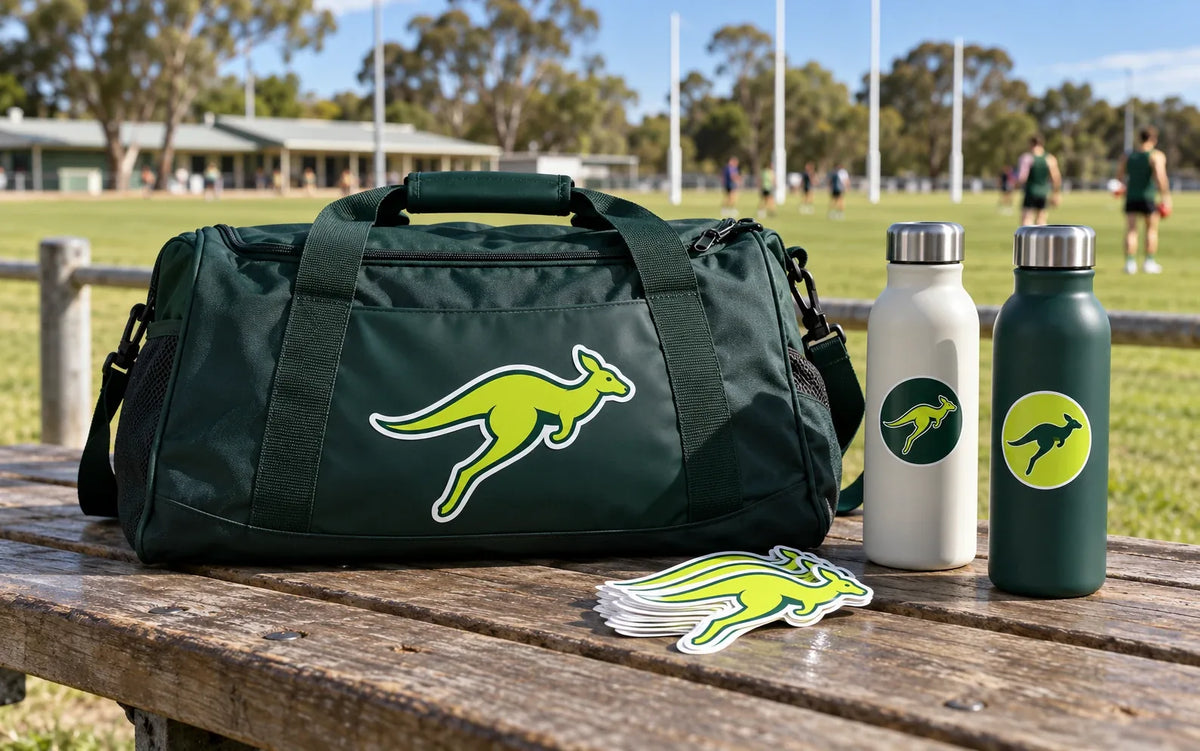 Dark green kit bag and two drink bottles with kangaroo mascot stickers on a bench beside a local footy oval